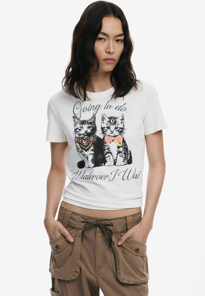 T-shirt en coton blanc avec un graphique de deux chats ornés d'accessoires colorés, avec le texte "Je vais faire ce que je veux." Manches courtes.
