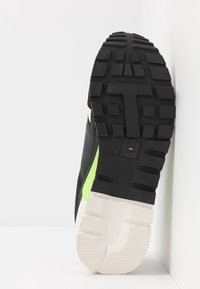 Černé tenisky s texturovanou gumovou podrážkou, s zeleným akcentem na boku a bílou mezipodešví. Vzor dezénu je silný a hluboký.