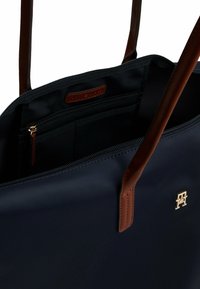 Borsa a spalla blu navy con un esterno in tessuto liscio, dettagli in pelle marrone, accessori in oro e una tasca interna con zip. Design spazioso, logo minimalista.