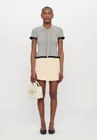 Top de manga corta a rayas en blanco y negro con cintura ajustada, combinado con una falda mini beige. Sosteniendo un pequeño bolso blanco. Zapatos planos negros.