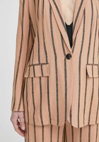 Blazer a righe grigie con strisce verticali nere; presenta due tasche frontali, rever a punta e chiusura con un singolo bottone. Tessuto testurizzato.