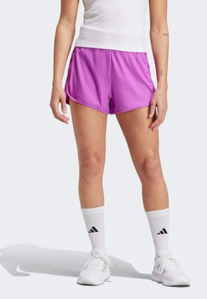 Shorts de sport plissés violets avec poches latérales, associés à des chaussettes blanches montantes avec un logo noir et des baskets blanches.