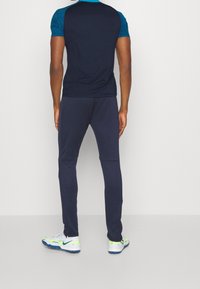 Dunkelblauses Sporthemd mit einer strukturierten blauen Muster-Oberfläche, kombiniert mit passenden marineblauen Hosen und weißen Sneakers mit grünen Akzenten.