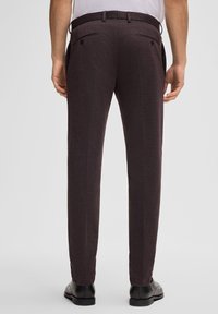 Dunkelburgunderfarbene maßgeschneiderte Hose mit glatter Textur, ausgestattet mit zwei Gesäßtaschen und dezenten Falten, kombiniert mit schwarzen Schuhen.
