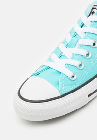 Baskets en toile bleu clair avec lacets blancs, embout en caoutchouc et bande noire le long de la semelle. Détail de surface texturée visible.