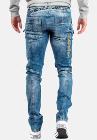 Jeans in denim blu chiaro con cuciture visibili, molteplici tasche e marchio sul retro. Texture liscia con un aspetto sbiadito.