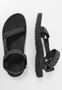 Svarte sandaler med teksturerte gummisåler, med justerbare vevde stropper i et geometrisk mønster. Enkel og funksjonell design.