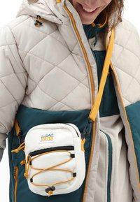Borsa a tracolla in felpa bianca con cerniera nera, dettagli gialli e tracolla regolabile; presenta un dettaglio con cordino elastico anteriore e patch con logo.