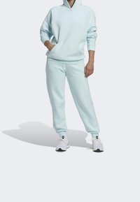 Sweat à capuche bleu clair avec une poche avant et des poignets côtelés, accompagné d'un pantalon de jogging assorti. Le matériau semble doux ; des baskets blanches complètent la tenue.