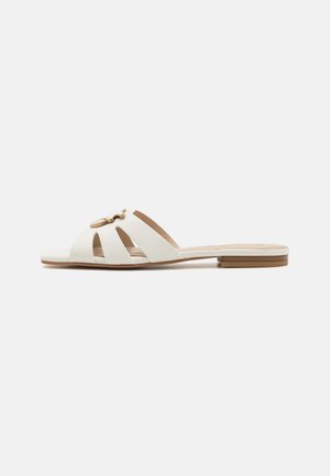 White slide sandals with cut-out design, flat sole, and gold-tone hardware accent. Smooth leather texture, featuring a minimalistic style.