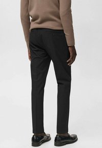 Pantalones negros a medida de tela suave, con corte Slim, bolsillo trasero y perneras rectas, combinados con mocasines negros.