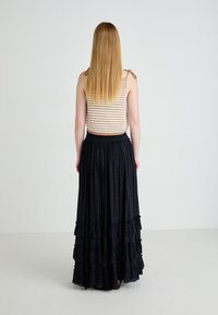 Haut rayé beige et blanc avec des bretelles ; longue jupe noire avec des couches volantes et un motif texturé ; mannequin de dos contre un fond uni.