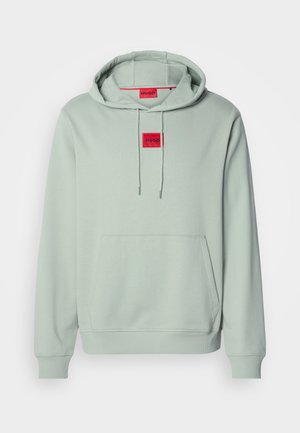 Svetlo zelena pulover kapuca z sprednjim kenguru žepom in rdečimi "HUGO" logotipnimi nalepkami na prsih in znotraj ovratnika.