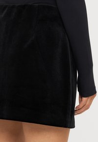 Melna samta svārki ar gludu tekstūru un strukturētu formu, kas piedāvā vidēja augstuma jostasvietu un sānu šuvju kabatas.
