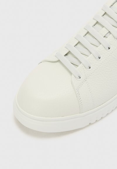 Baskets blanches en cuir avec un dessus texturé, bout rond et lacets gris. Possède un col rembourré et une semelle en caoutchouc blanche.