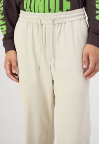Lyse beige ribbede joggebukser med elastisk midje og snor. Har lommer på siden og et teksturert stoff for komfort.