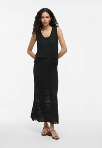 Haut sans manches en tricot noir avec un décolleté en dentelle associé à une jupe longue assortie présentant un motif en dentelle et un ourlet évasé.