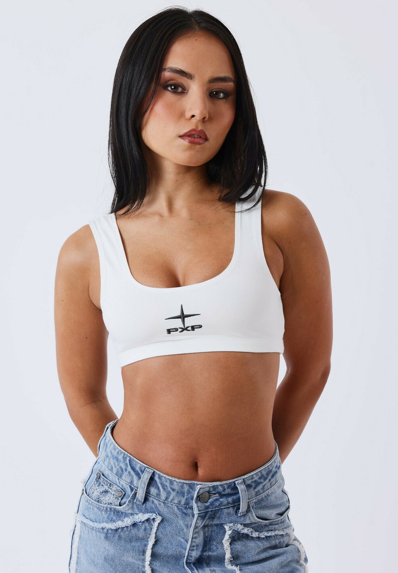 Cropped top bianco con scollo a quadrato e spalline sottili, caratterizzato da un logo "PXP" nero centrato sul petto. Indossato con pantaloni shorts in denim strappati.