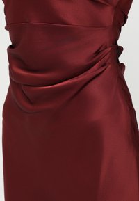 Burgundi sametkleit sujuva tekstuuriga, millel on kogutud detailid vöökohal ja külgseintel, luues figuuri järgiva silueti.