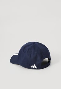 Marinehatt med buet skjerm, laget av stoff. Har et hvitt tre-stripes design på siden og et justerbart belte bak.