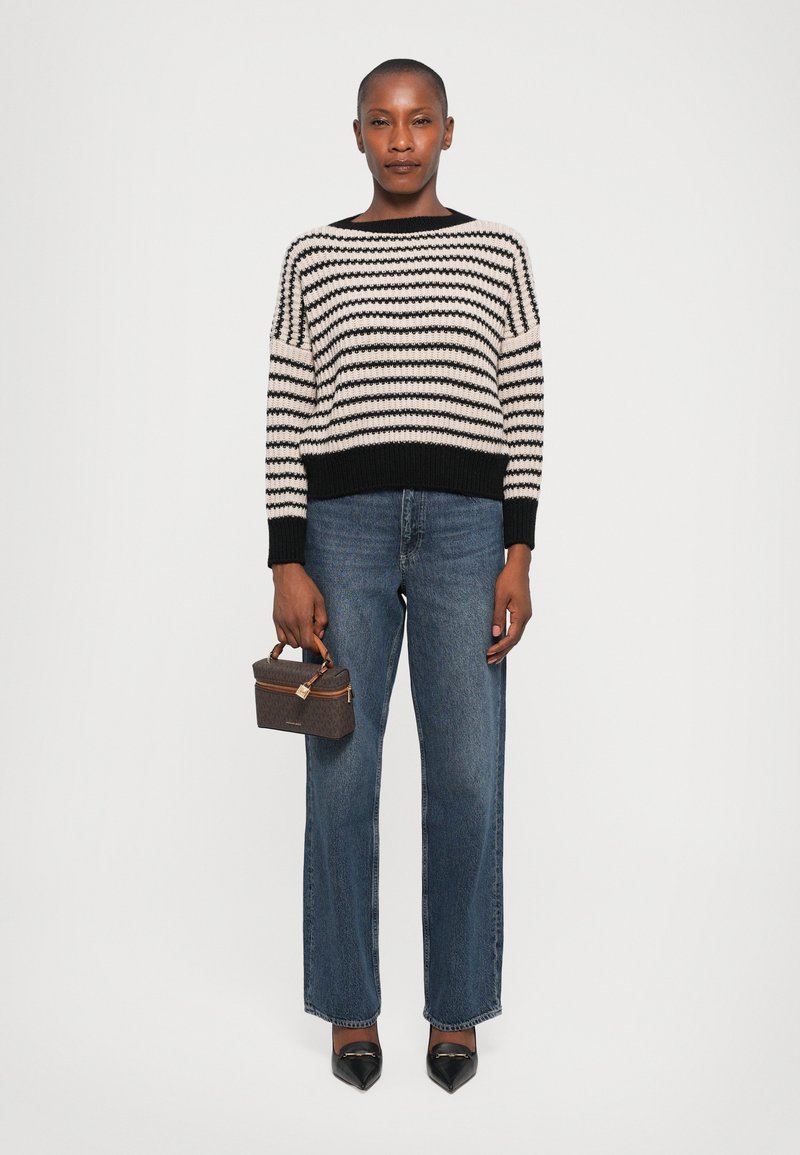Maglione a righe nere e crema con maniche ampie, abbinato a jeans blu a vita alta con gamba dritta. Tieni in mano una piccola borsa marrone. Tacchi neri.