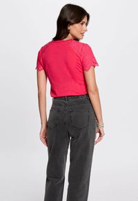 Camisa rosa ajustada con mangas de encaje de ojo de cerradura decorativas; combinada con pantalones vaqueros negros de cintura alta con bolsillos traseros y un corte recto.