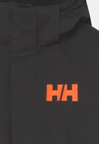 Černá bunda s vysokým límcem, s výrazným oranžovým logem "HH". Hladká textura s prošívaným švem. Žádné viditelné kapsy.
