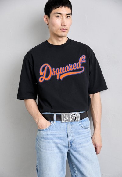 Melna kokvilnas t-krekla  ar sarkano un zilo "Dsquared²" logo, kombinēta ar gaiši ziliem džinsu biksēm un melnu jostu ar metāla "KISS" sprādzi.