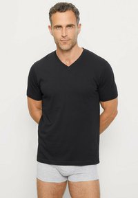 T-shirt di cotone nero con scollo a V e maniche corte, abbinato a pantaloni boxer grigi. Texture liscia, design aderente.