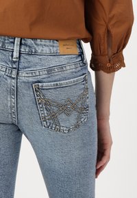 Jeans de denim azul claro con intrincadas costuras amarillas en los bolsillos traseros, que presentan una etiqueta de cuero con la inscripción "perfect jeans" en relieve.