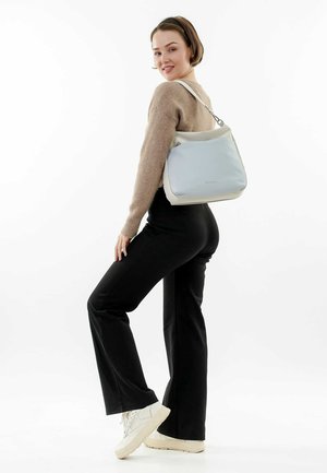 Sac à épaule bleu clair et crème en matériau lisse, présentant une forme simple et un design bicolore, porté avec une tenue décontractée.