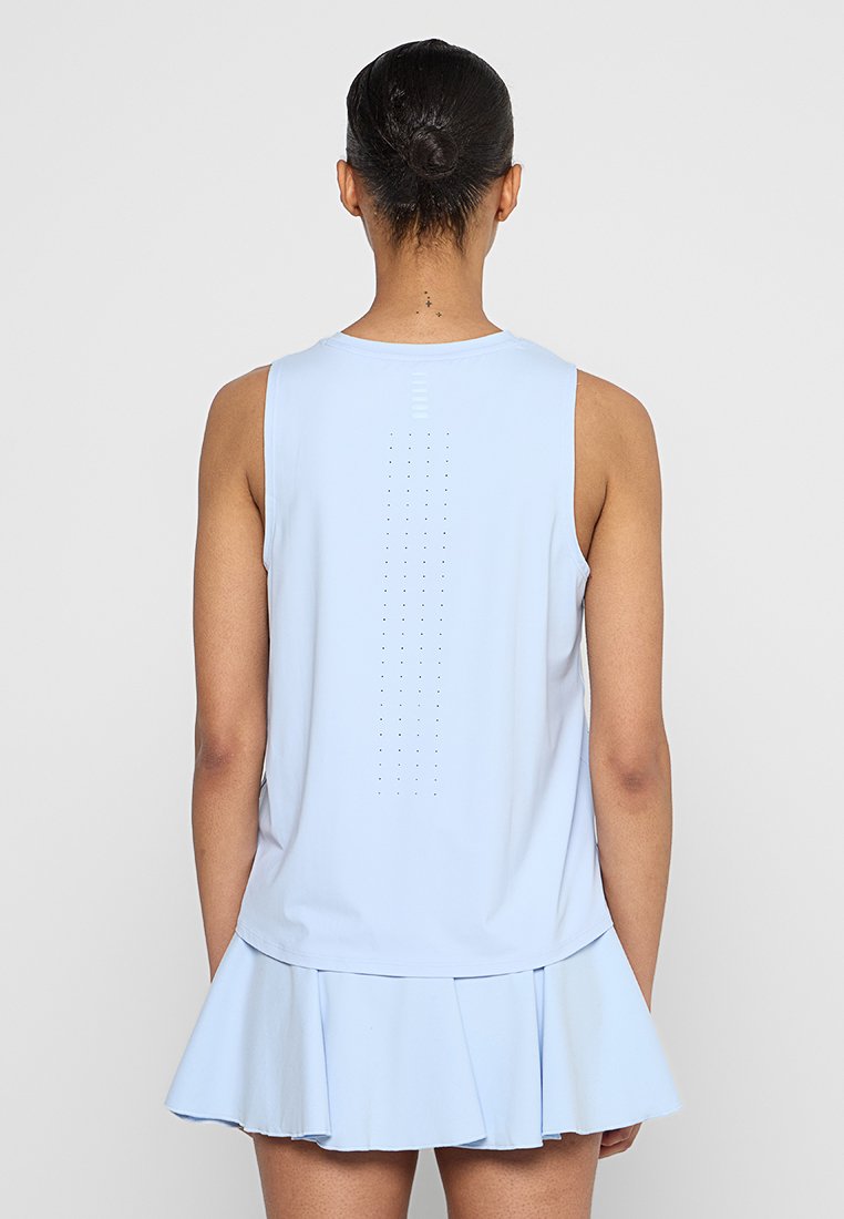 Mujer con el cabello recogido en un moño, que lleva puesta una blusa sin mangas de color azul claro con perforaciones verticales y una falda plisada a juego, de espaldas.