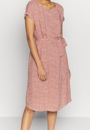 Woman wearing a knee-length, short-sleeve pink dress with small white floral pattern and a tied waist belt.