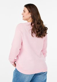 Maglione texture rosa chiaro con maniche lunghe e scollatura rotonda, abbinato a jeans di denim blu. Accenti a coste sottili ai polsini e all'orlo.