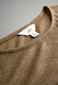 Rudas megztas audinys su apvaliu iškirpimu ir baltu drabužių etiketė „THE SET“, dydis vidutinis, pagaminta Bangladeše.