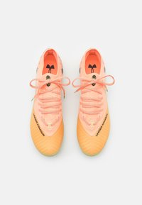 Scarpe da ginnastica arancioni e rosa con una tomaia a fantasia, suola texturizzata e logo nero. Presentano lacci e elementi di design distintivi.