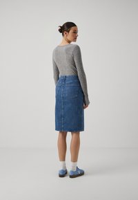 Haut gris à manches longues à côtes associé à une jupe crayon en denim bleu avec deux poches arrière et une silhouette ajustée. Des chaussures bleues complètent la tenue.