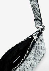 Snakeskin pattern bag in black and white, featuring a silver zipper and hardware, with a black fabric interior and side strap attachment.