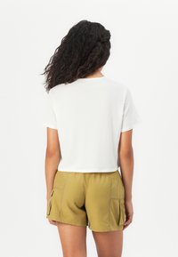 T-shirt blanc raccourci à manches courtes associé à un short cargo vert olive clair avec poches latérales et tissu texturé.