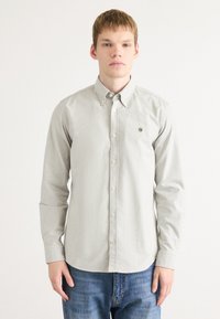 Lys grå knapp-up skjorte med spiss krage, lange ermer, og en liten logoaccent. Kombinert med blå denimjeans.