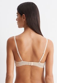 Beige bh met verstelbare bandjes, gladde stof en een haak-en-oogsluiting aan de achterkant. Heeft een minimalistisch ontwerp zonder versieringen.