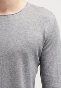 Maglietta grigia a maniche lunghe con scollatura rotonda, realizzata in un tessuto morbido ed elastico con una texture liscia e senza motivi o dettagli visibili.