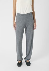 Graue, weiche Strickhose mit entspannter Passform und elastischem Bund, kombiniert mit schwarzen Slippern. Der Stoff wirkt glatt und warm.