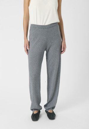 Pantaloni grigi in maglia morbida con vestibilità rilassata e vita elastica, abbinati a scarpe nere slip-on. Il tessuto appare liscio e caldo.