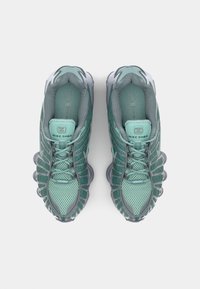 Zapatillas deportivas de malla verde con un diseño texturizado, que cuentan con una media suela con muelles distintivos, acentos grises y una lengüeta acolchada.