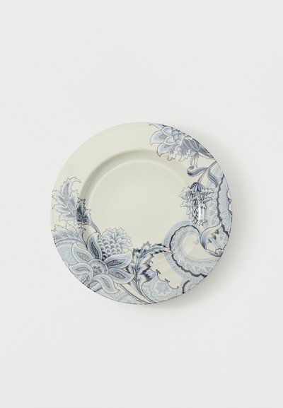 Assiette en céramique blanche avec des motifs floraux et paisley bleus décorant le bord sur un fond blanc uni.