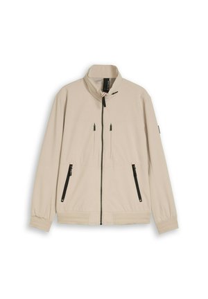 Veste beige zippée avec col montant, détails de fermeture éclair noirs sur les poches avant et la poitrine, poignets élastiques et ourlet côtelé.