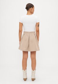 Falda plisada beige hecha de tejido texturizado, combinada con una camiseta blanca de canalé. Modelo vistiendo botas de vaquero color crema, visto desde detrás.