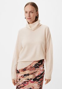 Jasnoróżowy sweter z golfem i prążkowanymi mankietami, o luźnym kroju. Połączony z wzorzystą, wielokolorową spódnicą.