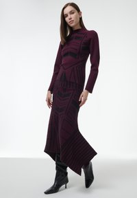 Conjunto de suéter y falda de punto en color marrón, con patrones geométricos en negro, mangas largas y un dobladillo asimétrico. Textura suave, diseño ajustado.